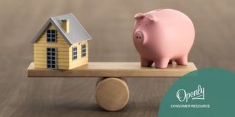 A toy piggy bank is balanced on a scale with a miniature house.
