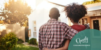 A man and woman embrace while looking at a house.