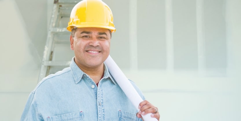 A smiling man wearing a hardhat hold a pipe.