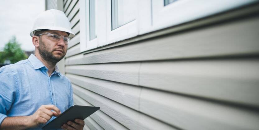 A man inspects the siding of a house. 