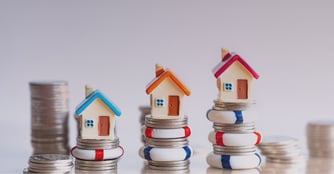 Miniature houses stacked on increasingly larger piles of coins