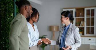 A smiling Black couple shakes hands with a female business professional in a bright office, symbolizing a successful partnership.