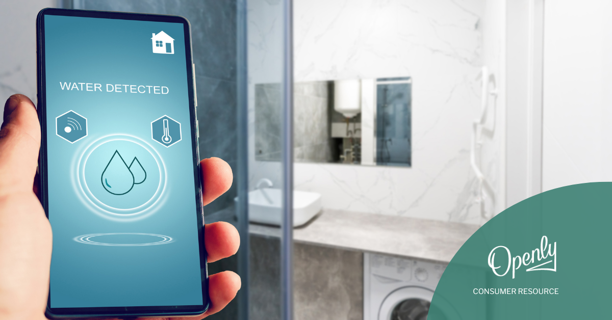 An adult is holding a cell phone displaying a water detection alert in a bathroom. 
