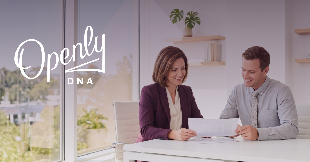 A smiling man and smiling woman sit at a desk looking at paperwork. 